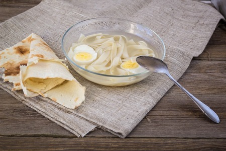 cup of chicken soup with noodles and eggs and pita breadの写真素材