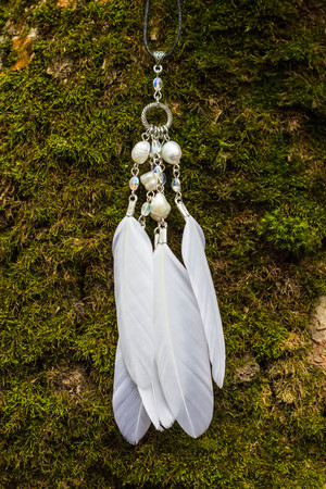 White pendant with feathers and beads in the forest, handmade.の写真素材