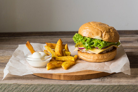 Home made hamburger with chicken, onion, cucumber, lettuce and cheese on wooden rustic table with potato friesの写真素材
