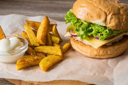 Home made hamburger with chicken, onion, cucumber, lettuce and cheese on wooden rustic table with potato friesの写真素材