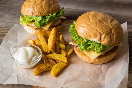 Home made hamburger with chicken, onion, cucumber, lettuce and cheese on wooden rustic table with potato friesの写真素材