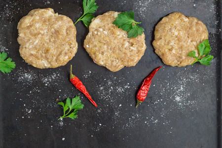 raw burgers - cutlets from chicken meat with parsley and chili peppers on a black background, top viewの写真素材