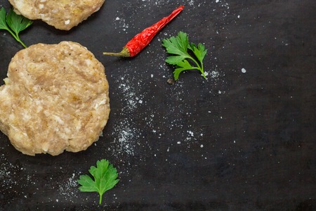 raw burgers - cutlets from chicken meat with parsley and chili peppers on a black background, top viewの写真素材