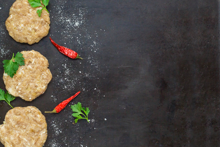 raw burgers - cutlets from chicken meat with parsley and chili peppers on a black background, top viewの写真素材
