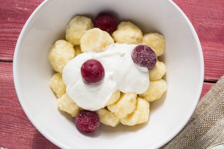 Traditional russian, ukrainian cottage cheese lazy dumplings served with sour cream and cherry on wooden backgroundの写真素材