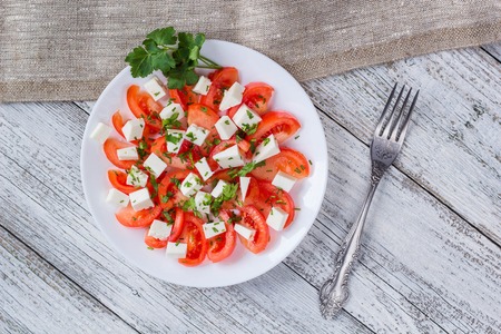 Fresh salad with tomato, mozzarella and herbs on white wooden backgroundの写真素材