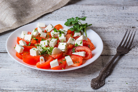 Fresh salad with tomato, mozzarella and herbs on white wooden backgroundの写真素材