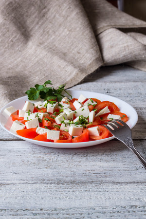 Fresh salad with tomato, mozzarella and herbs on white wooden backgroundの写真素材