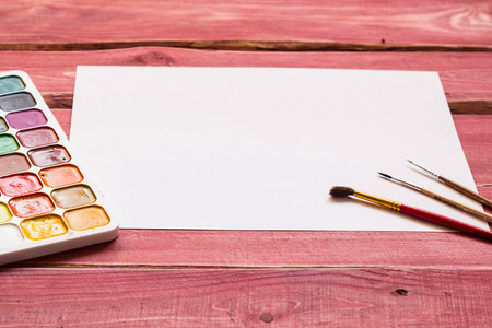 Artistic mockup with empty white sheet of paper and art supplies around including watercolor and brushesの写真素材
