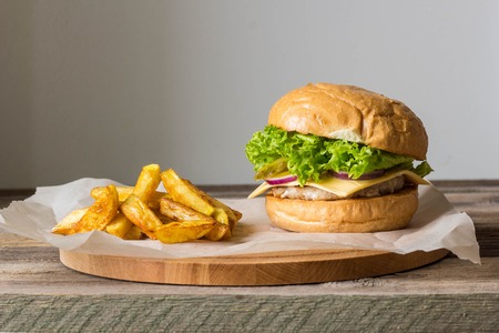 Home made hamburger with chicken, onion, cucumber, lettuce and cheese on wooden rustic table with potato friesの写真素材