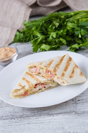 shawarma in thin pita bread with chicken and vegetables on a white plateの写真素材