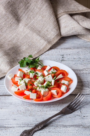 Fresh salad with tomato, mozzarella and herbs on white wooden backgroundの写真素材