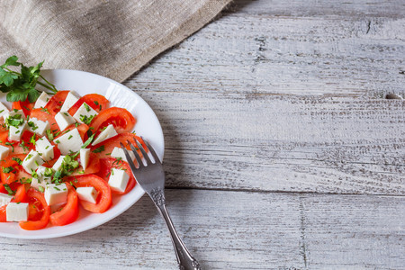 Fresh salad with tomato, mozzarella and herbs on white wooden backgroundの写真素材