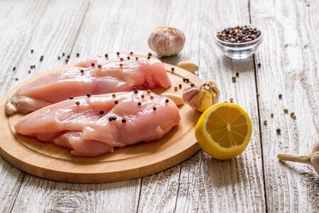 Raw chicken breasts with lemon pepper and garlic on wooden backgroundの写真素材
