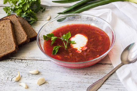 Vegetables and meat in red beetroot soup or borsch with sour cream. bread, green onion, parsley, garlic around the plate with metal spoonの写真素材
