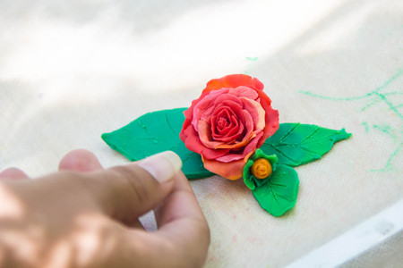 a plasticine pink rose with green leaves with hand on light backgrounの写真素材