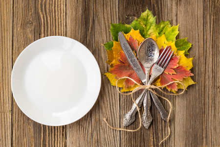 Autumn Table setting. Thanksgiving dinner plate with fork, knife and leaves on rustic wooden table background. Top view, copy space, place for text.の写真素材