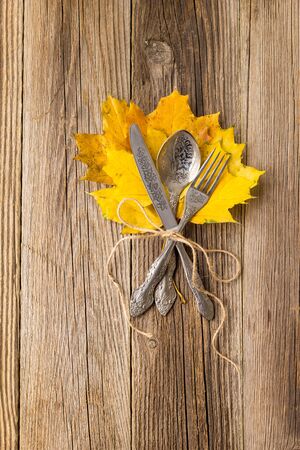 Autumn dinner place setting for Thanksgiving holiday with colorful maple leaves on rustic wooden boards.の写真素材