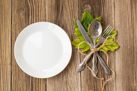Autumn Table setting. Thanksgiving dinner plate with fork, knife and leaves on rustic wooden table background. Top view, copy space, place for text.の写真素材