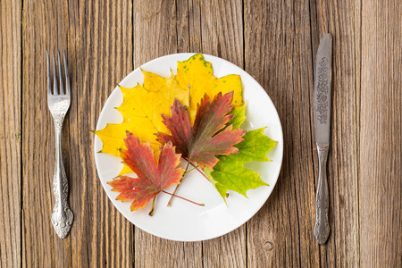 Autumn Table setting. Thanksgiving dinner plate with fork, knife and leaves on rustic wooden table background.の写真素材