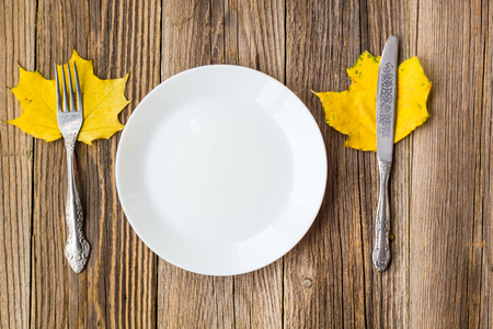 Autumn Table setting. Thanksgiving dinner plate with fork, knife and leaves on rustic wooden table background. Top view, copy space, place for text.の写真素材