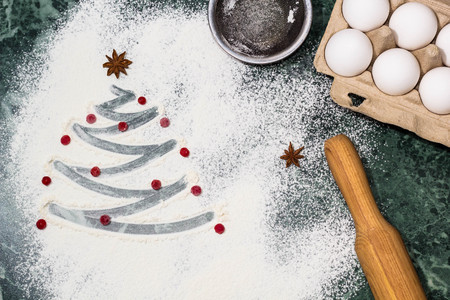 Ingredients for cooking christmas baking. Christmas tree with the flour, berries and anise star spices as a decoration and rolling pin, eggs, strainerの写真素材
