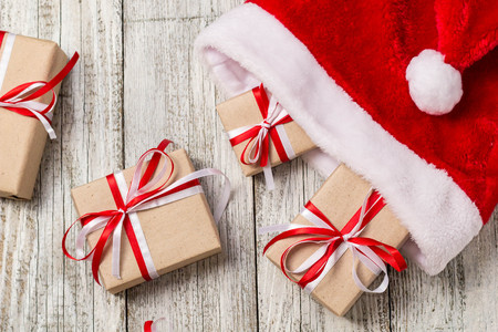 Top view of santa hat with christmas gift boxes on white wooden background.の写真素材