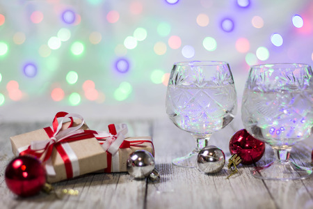 Two glasses of christmas champagne with gift boxes and balls decorations against light bokeh background.の写真素材