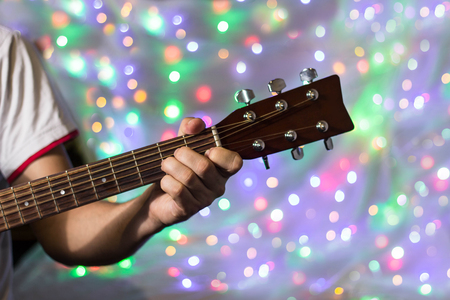 Man playing on acoustic guitar. Closeup fingers on guitar neck against christmas blurred bokeh lights on background.の写真素材
