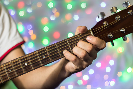 Man playing on acoustic guitar. Closeup fingers on guitar neck against christmas blurred bokeh lights on background.の写真素材