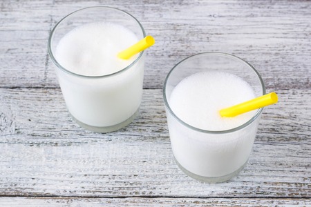 Glasses of milk with yellow straws on white wooden background.の写真素材
