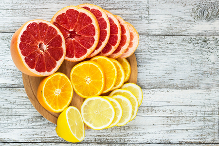 Sliced fresh citrus - lemons, grapefruits, oranges on a wooden cutting board with a knife.の写真素材