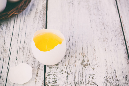Broke One whole egg amongst white eggs in basket on a white wooden background, tonedの写真素材