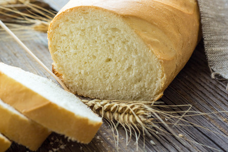 Sliced bread with wheat spikes on wooden table closeup.
