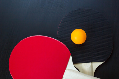 Two table tennis or ping pong rackets and ball on a black background.