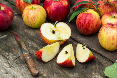 Red apple sliced and knife on old wooden table.