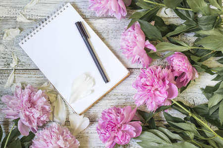 Open blank notepad, pen, and peony on the white wooden table. romantic flat lay