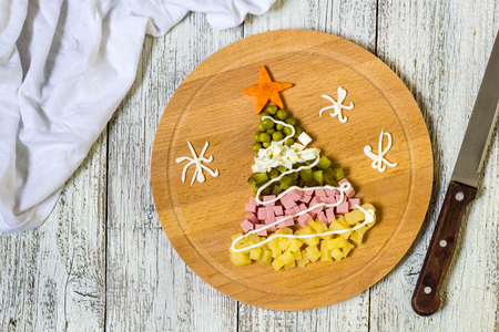 Christmas tree from a salad olivier on cutting Board on a white wooden table. Top view with a copy spaceの写真素材