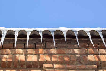 Wintry roof of the house with icicles on blue sky background.の写真素材