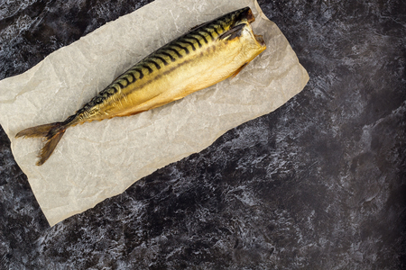 One smoked mackerel without head on baking paper on black background. copyspace top viewの写真素材