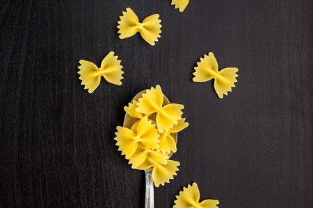 italian raw farfalle pasta dry on a metallic spoon and an dark black table
