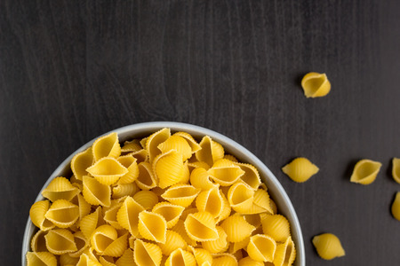 Top view of black background with italian raw conchiglie paste shells in grey bowl with copy spaceの写真素材