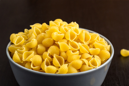 black background with italian raw conchiglie paste shells in grey bowl with copy space