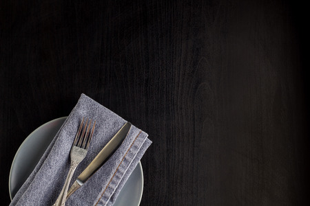 table setting with empty plate napkin fork and knife on black wooden background