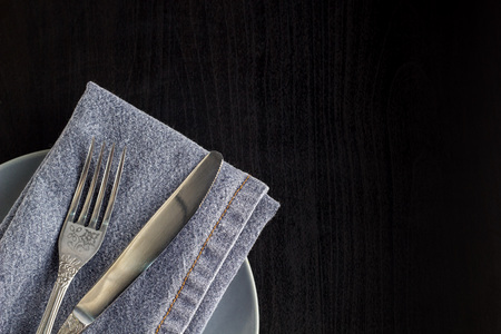 table setting with empty plate napkin fork and knife on black wooden backgroundの写真素材