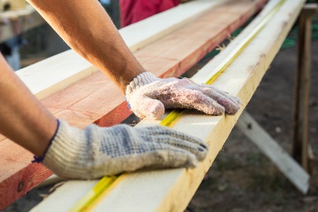 Close up view of a man hands measuring wooden plank with a tape line. Measurement. Building and maintenance.の写真素材