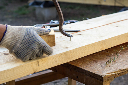 Carpenter pulling a nail from a plank using Claw hammer outdoor