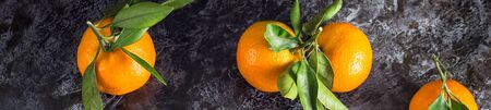 Border of Many orange tangerines with green leaves on dark background. Top view and copy space.