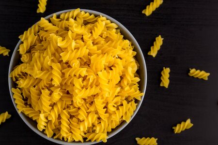 Top view of black background with italian rawpasta horns in grey bowl with copy space