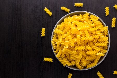 Top view of black background with italian rawpasta spiral fusilli in grey bowl with copy spaceの写真素材